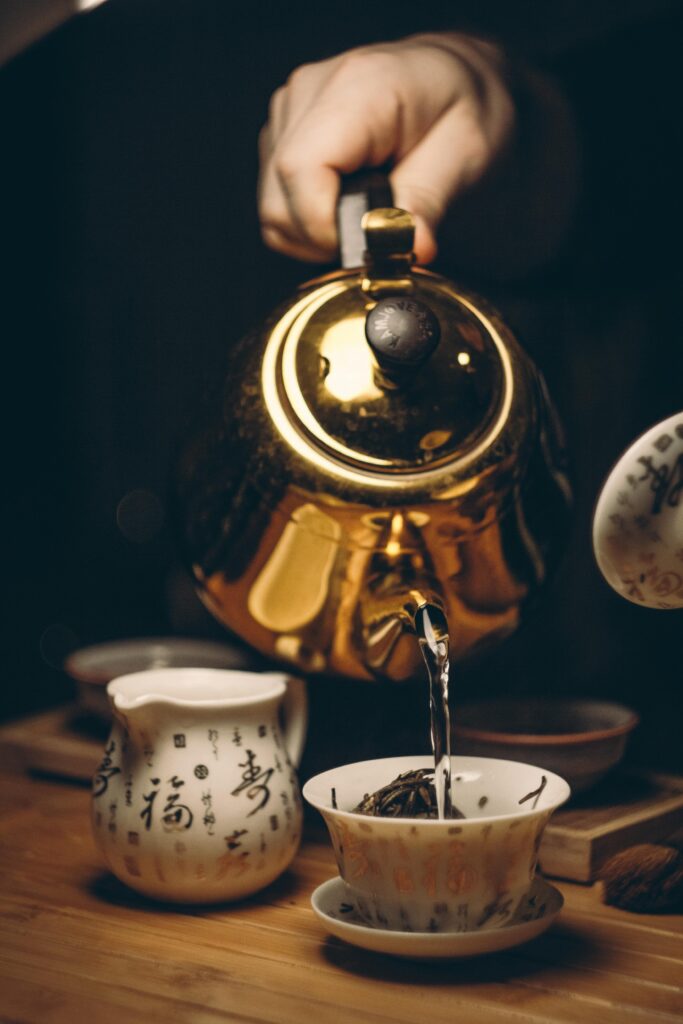 pexels-photo-230490-230490 Close-up of a golden teapot pouring tea into a cup with Chinese calligraphy.